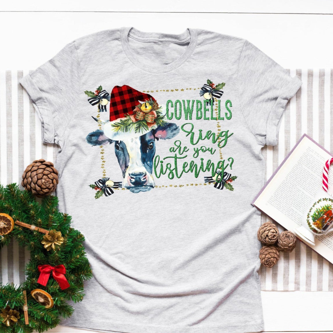 Gray t-shirt with Christmas-themed design featuring a reindeer and text, placed on a white surface with decorative items.