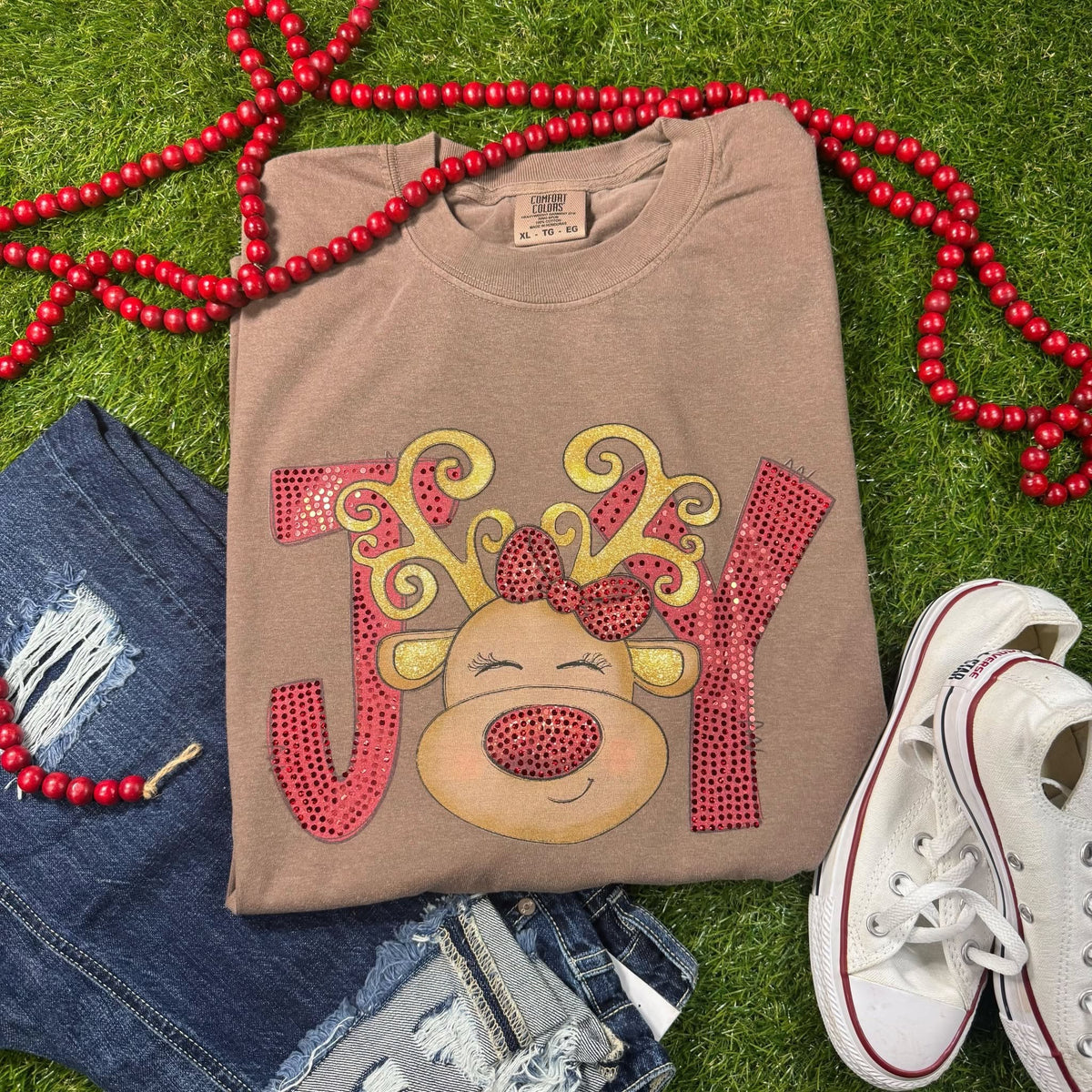 JOY reindeer Christmas design with red spangle lettering and bow on a brown Comfort Colors shirt